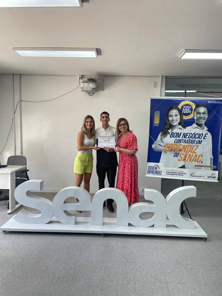 Micael Polini recebendo a premiação pelas mãos da Vice Presidente Luciane Trindade e companheira Carla, responsável pelo desenvolvimento do projeto.