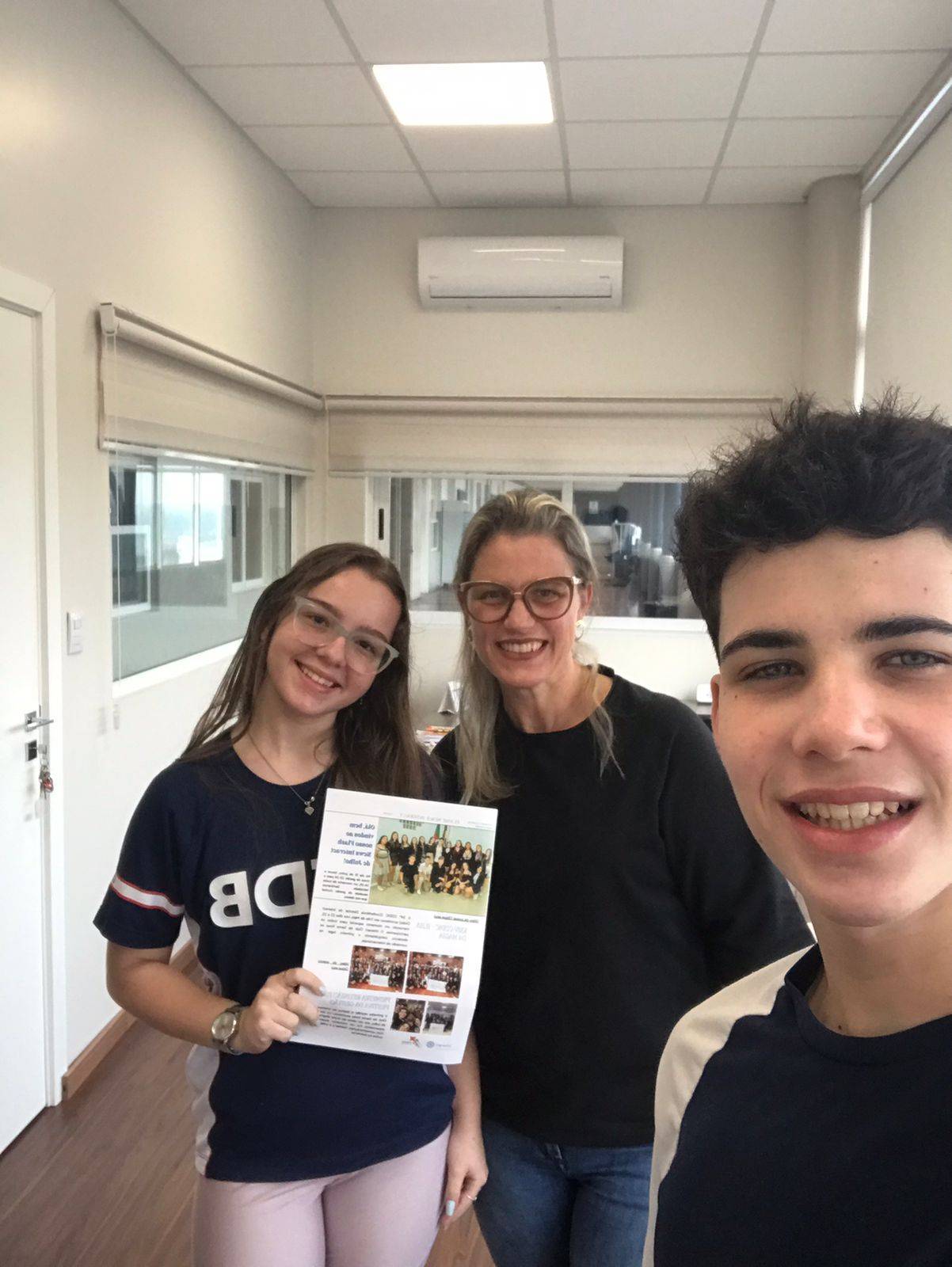 Presidente e diretora de imagem pública do Interact Club de Santa Rosa entregando o jornal "Flash News" a coordenadora do Colégio Salesiano Dom Bosco.