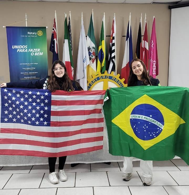 Giovana a esquerda com a bandeira dos EUA e Paula a direita com a bandeira do Brasil.